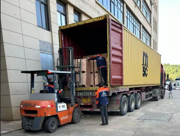 Operador de empilhadeira carrega caixas de madeira em um contêiner amarelo em um caminhão, com trabalhadores auxiliando em uma instalação industrial.
