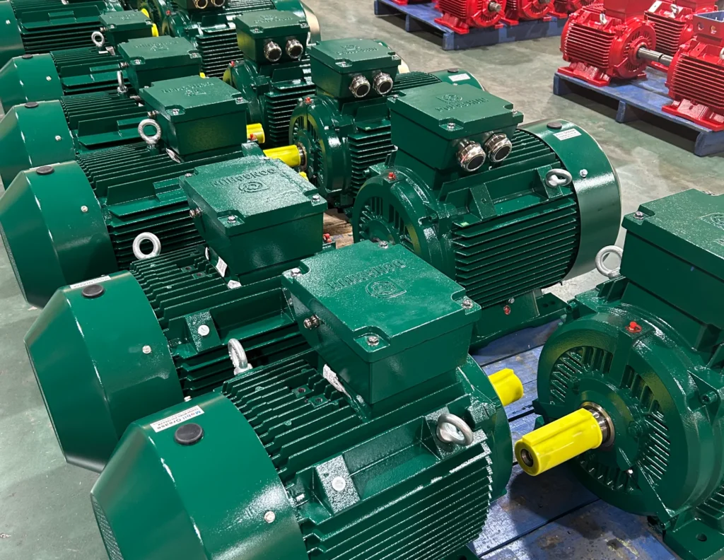 Rangées de moteurs électriques industriels verts et rouges organisés sur des palettes dans un entrepôt avec un ouvrier en arrière-plan.
