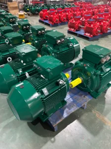 Several green and red industrial electric motors organized on pallets inside a warehouse.